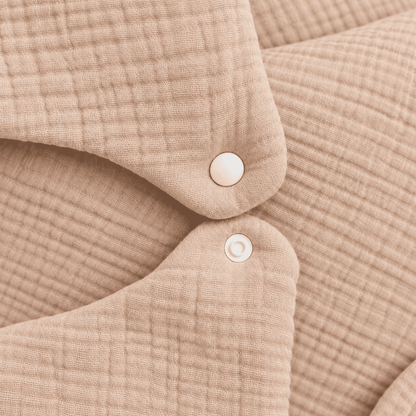 Close-up of a beige waffle-weave fabric garment with two white snap buttons, showing the textured material and soft folds.