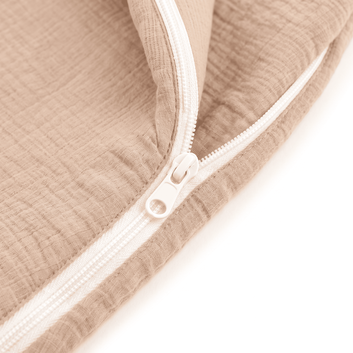 Close-up of a beige muslin fabric item with a white zipper, showing the textured fabric and zipper details against a white background.